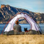 woman and a dog inside outdoor tent near body of water