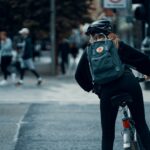 person in black jacket and black pants with green backpack riding on black motorcycle during daytime